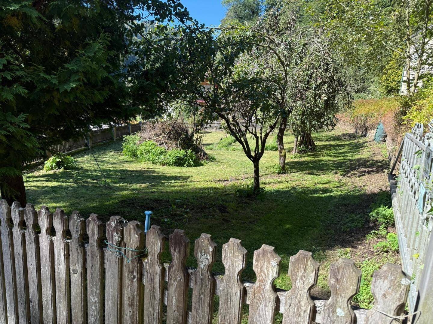 Gepflegter Gartenbereich mit Rasenfläche, Obstbäumen und rustikalem Holzzaun.