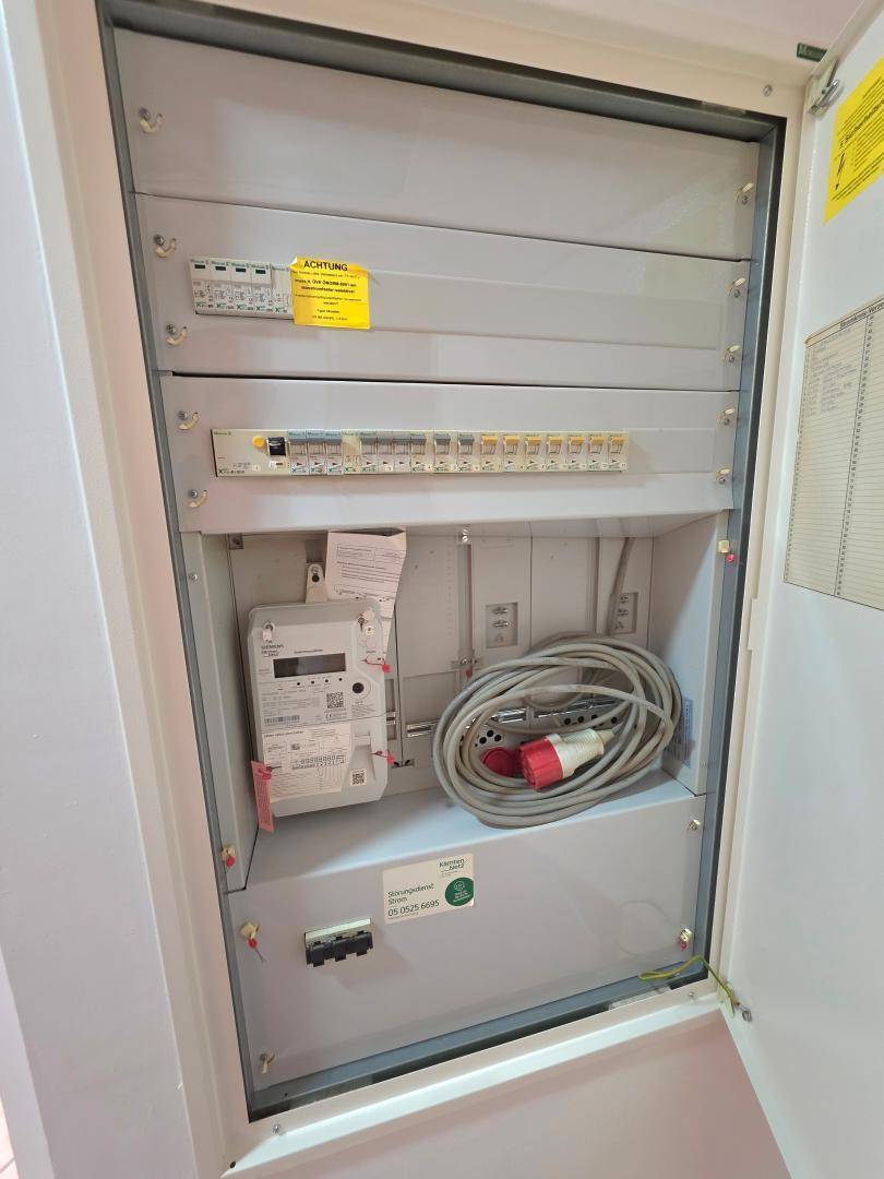 Elektrischer Verteilerkasten mit Sicherungen und Zähler in einem Technikraum.