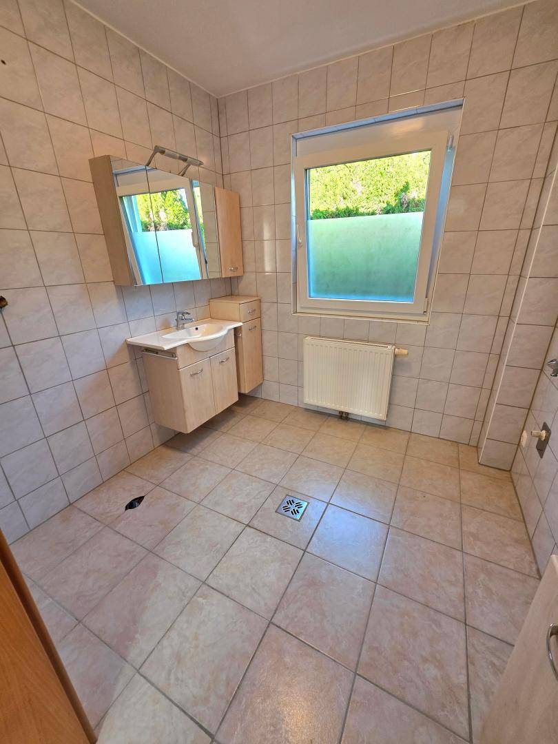 Gefliestes Badezimmer mit Einzelwaschbecken, Spiegelschrank und Fenster für Tageslicht.