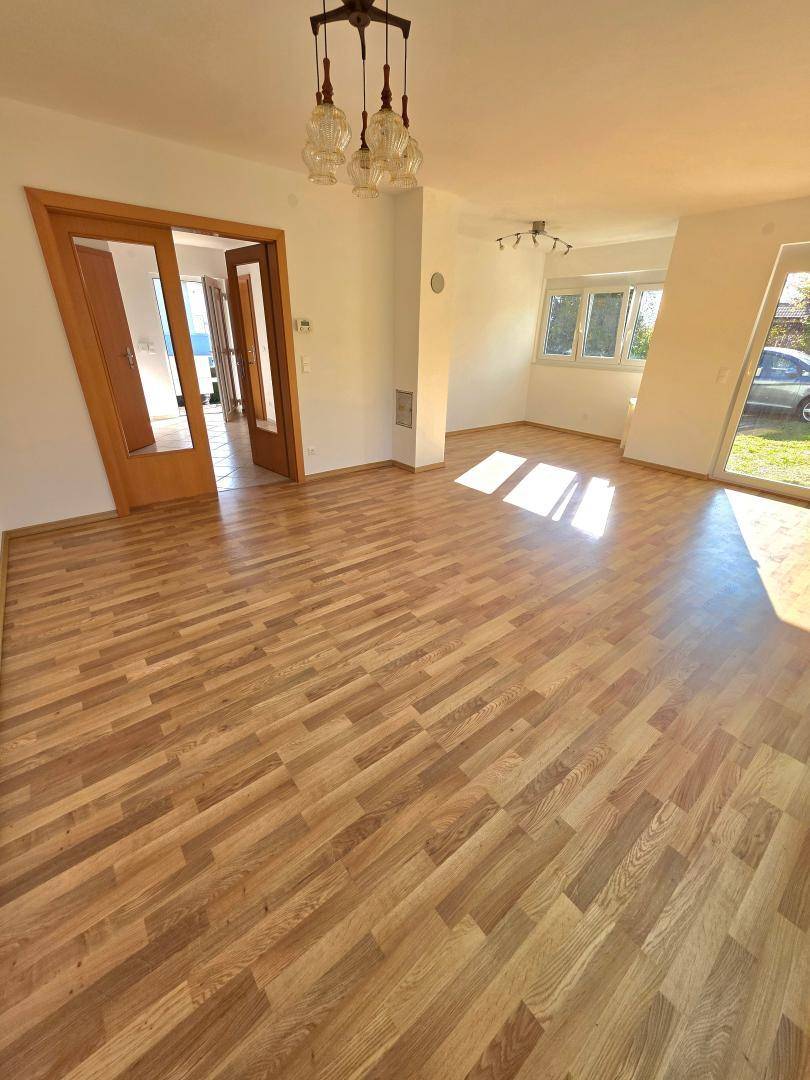 Helles Wohnzimmer mit Laminatboden und Zugang zum Garten durch große Glastüren.