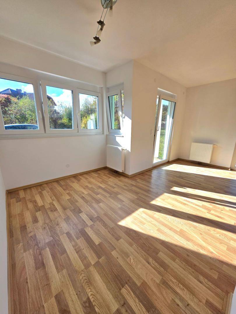 Lichtdurchfluteter Wohnbereich mit großen Fenstern und Heizkörpern unter den Fensterbänken.