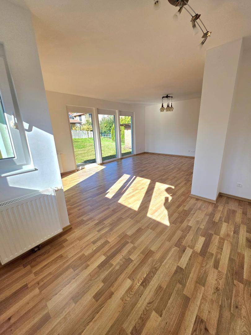Geräumiges Wohnzimmer mit Laminatboden, viel Tageslicht und Blick in den Garten.