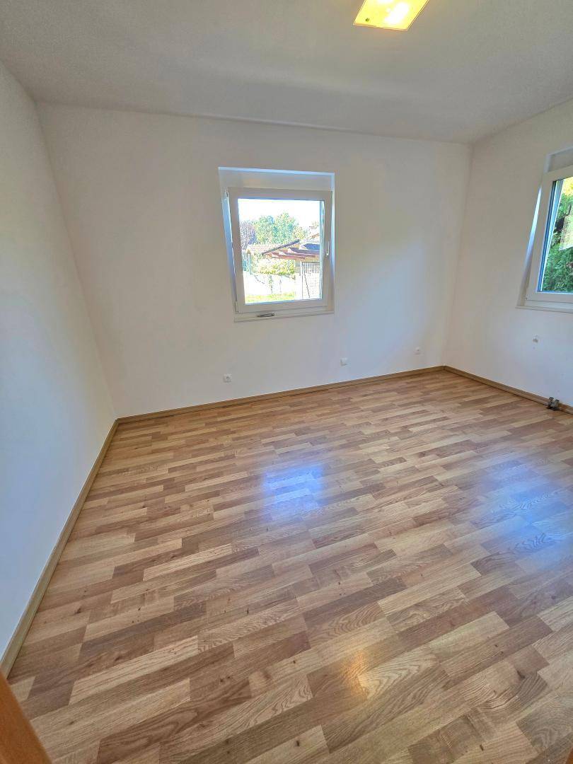 Schlafzimmer mit Laminatboden, weißen Wänden und zwei Fenstern für viel Licht.