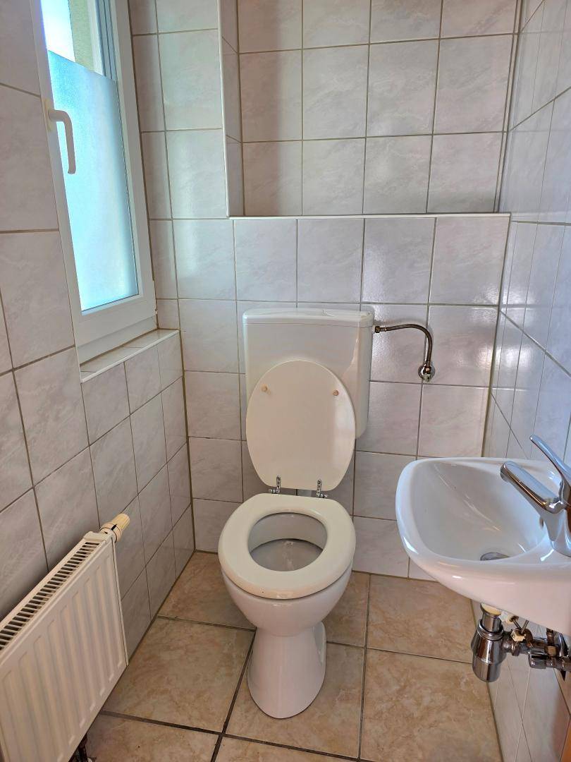 Kleines Gäste-WC mit Fliesen, Toilette, Waschbecken und Fenster.