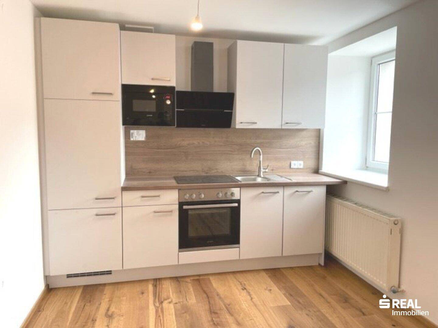 Moderne Einbauküche mit weißen Schränken, Holzdetails und integrierten Geräten.