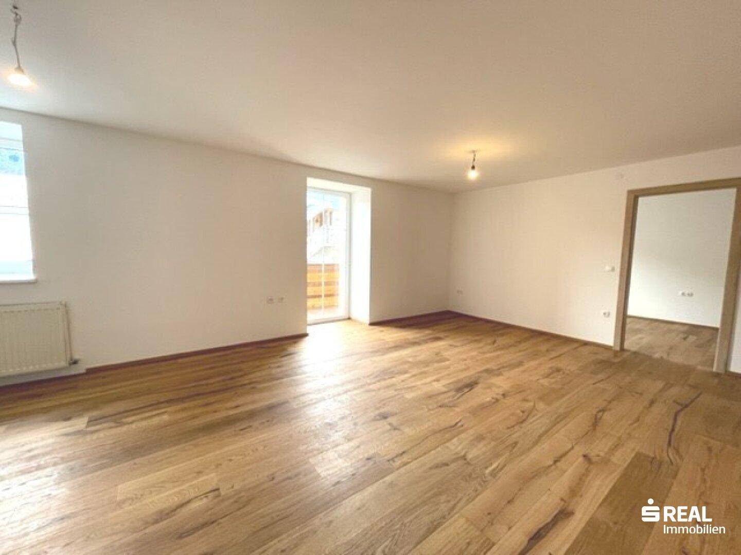 Geräumiger, heller Wohnbereich mit Holzboden und direktem Zugang zum Balkon.