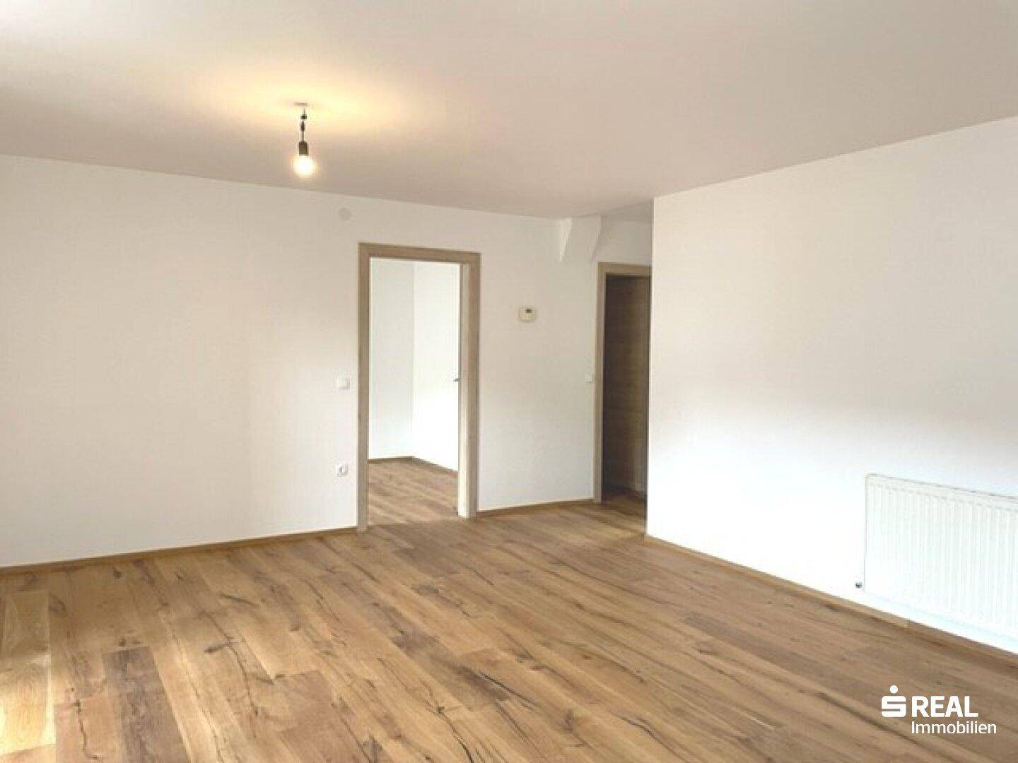 Heller Raum mit Holzboden und zwei Türen, die zu weiteren Zimmern führen.