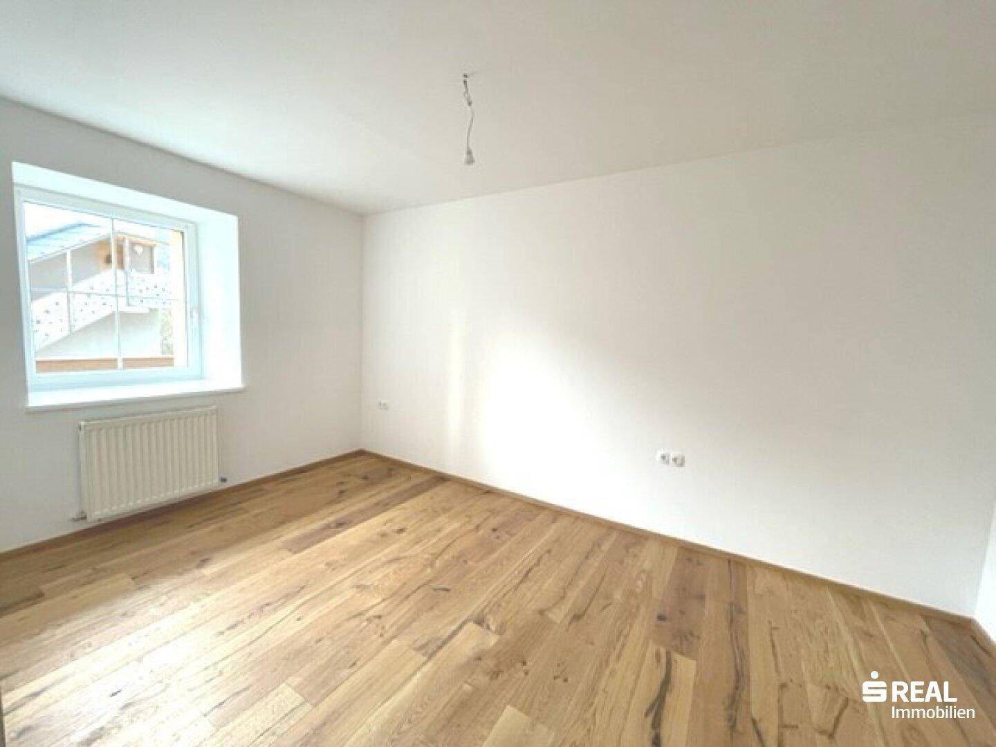 Helles Schlafzimmer mit Holzboden und einem Fenster, das viel Tageslicht hereinlässt.