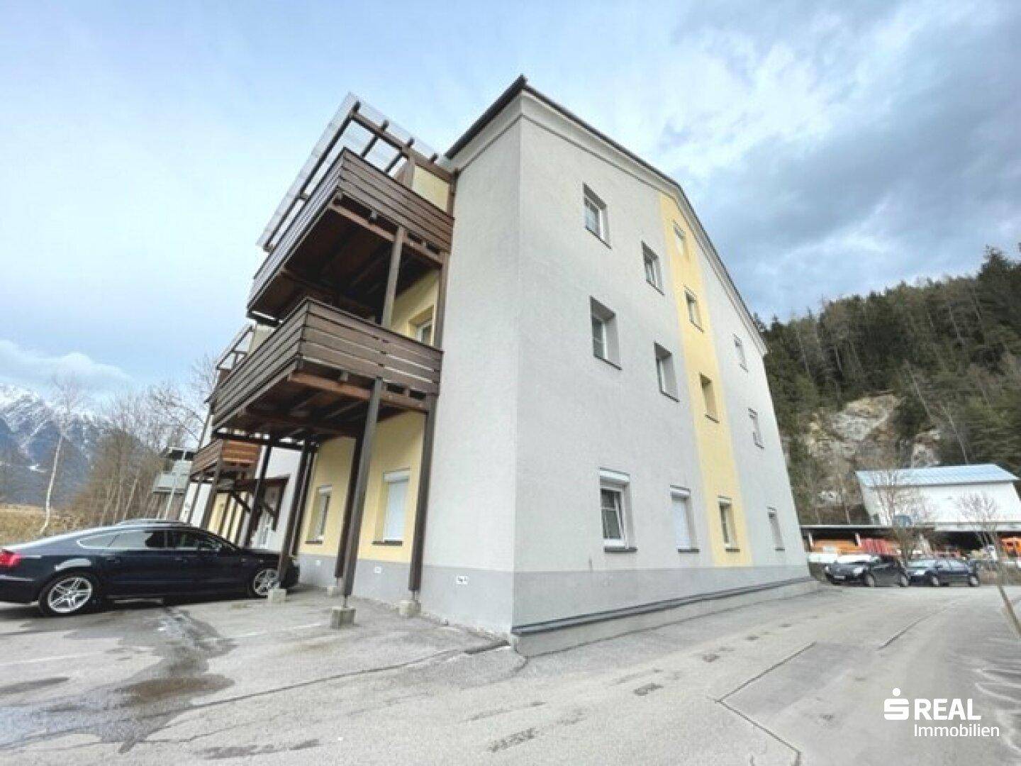 Mehrstöckiges Gebäude mit Balkonen und Parkplätzen, umgeben von einer Berglandschaft.