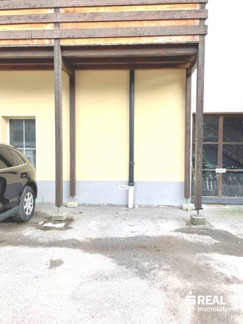 Detailansicht des Erdgeschosses mit überdachtem Parkplatz unter einem Balkon.