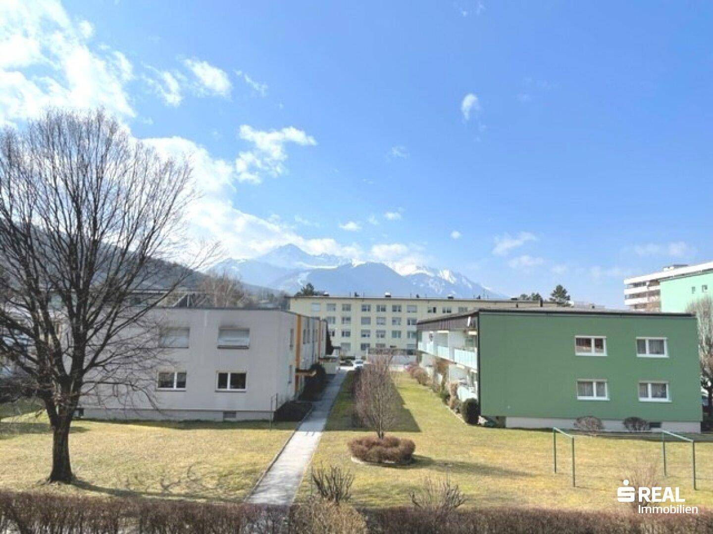 Außenansicht von Wohngebäuden mit grüner Rasenfläche und beeindruckendem Bergblick im Hintergrund.
