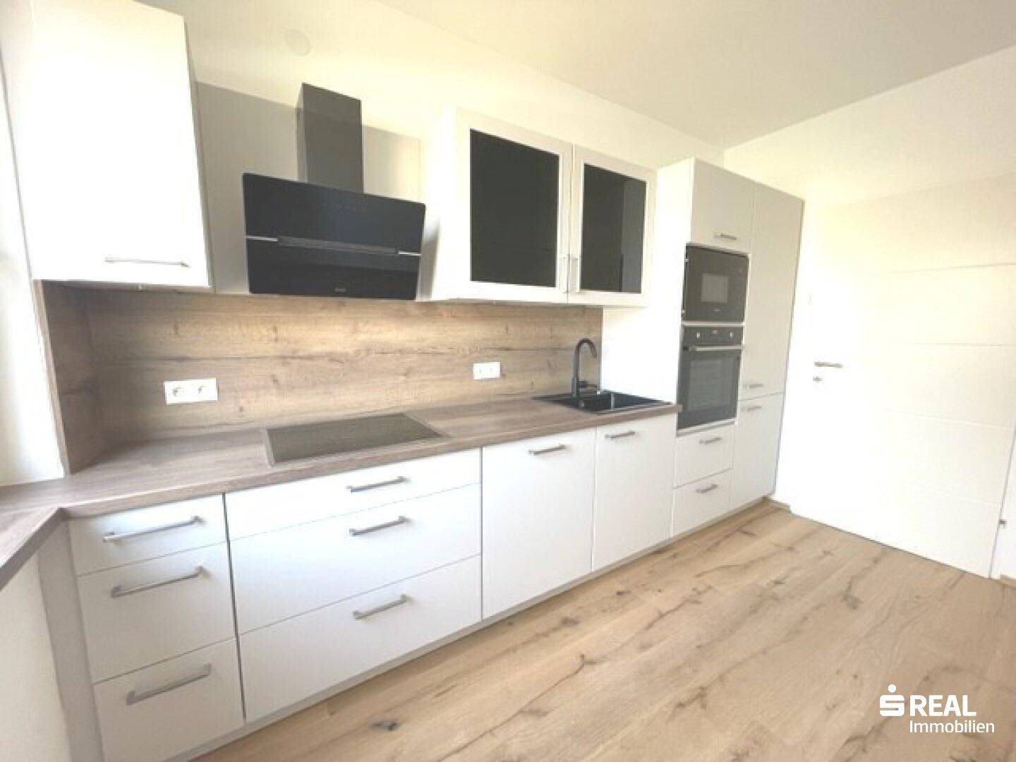 Helle Küche mit weißen Fronten, Holzoptik-Arbeitsplatte, Induktionskochfeld und Dunstabzugshaube.