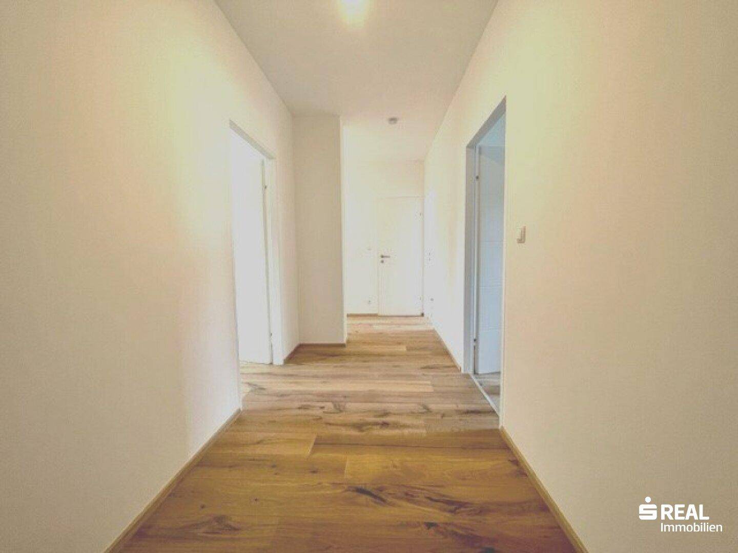 Heller Flur mit modernem Holzfußboden und weißen Wänden, der zu verschiedenen Räumen führt.