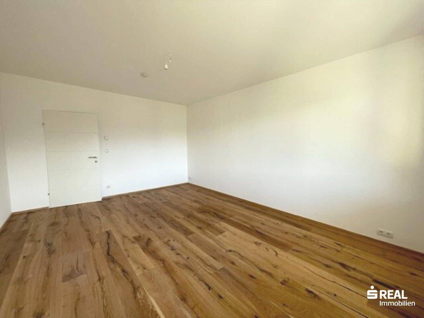 Geräumiger, leerer Raum mit weiß gestrichenen Wänden und einem attraktiven Holzfußboden.