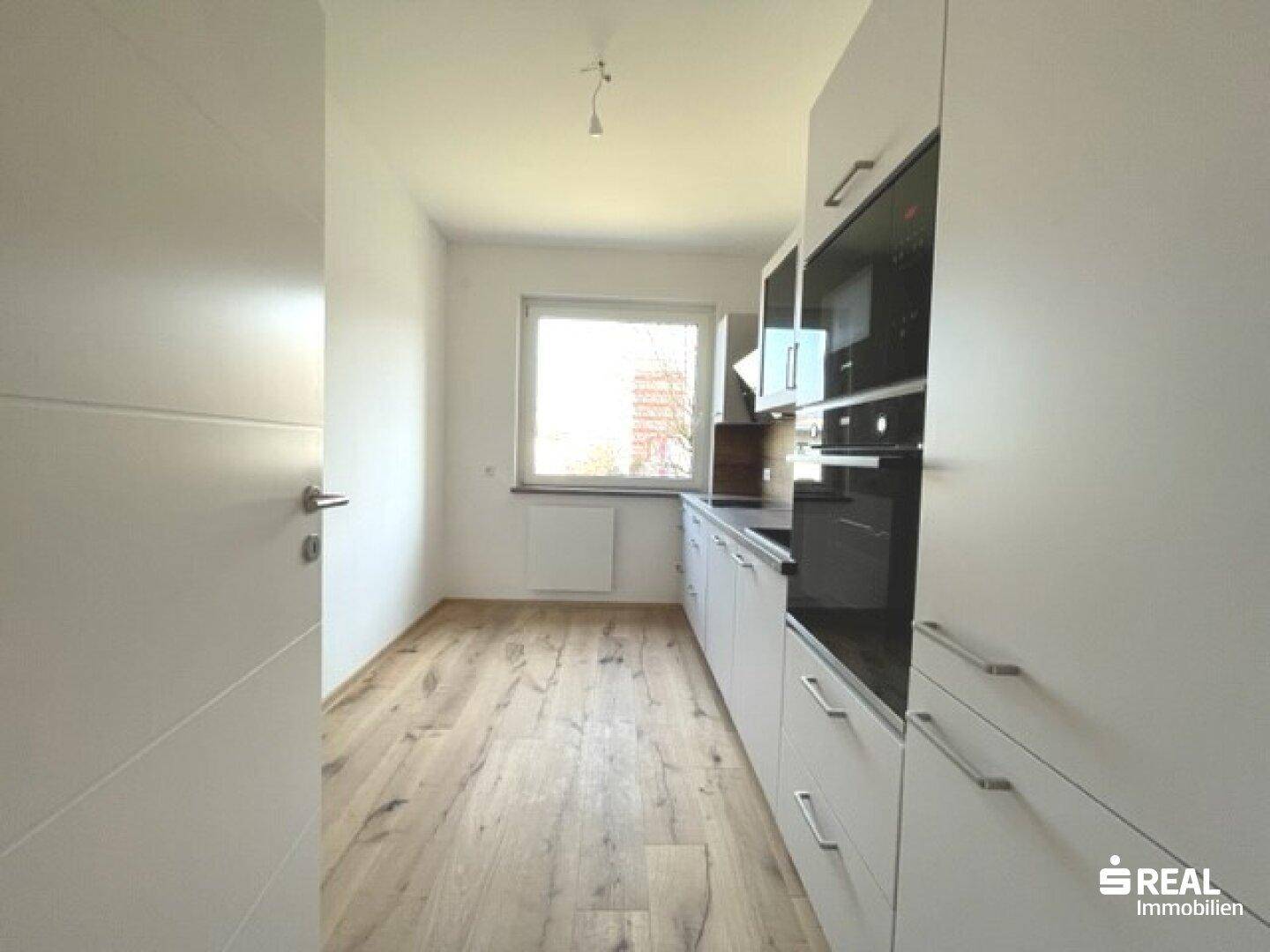 Eingangsbereich zur modernen Küche mit weißen Schränken, integrierten Geräten und hellem Holzfußboden.