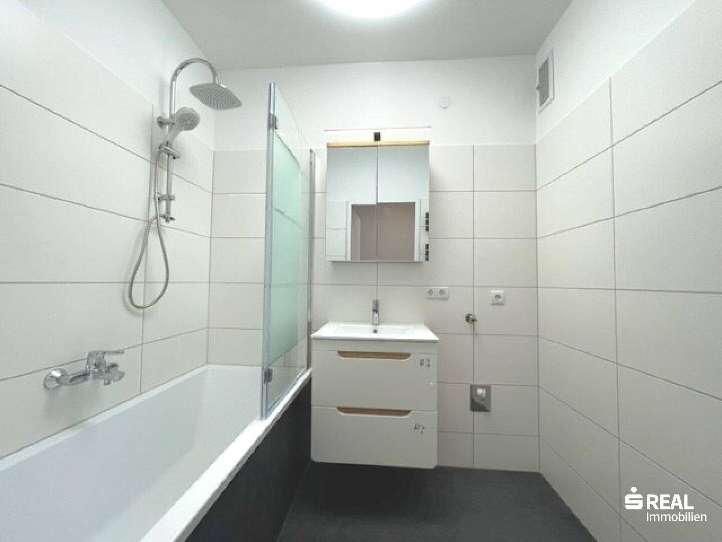 Modernes Badezimmer mit Badewanne, Duschfunktion, Einzelwaschbecken und weiß gefliesten Wänden.
