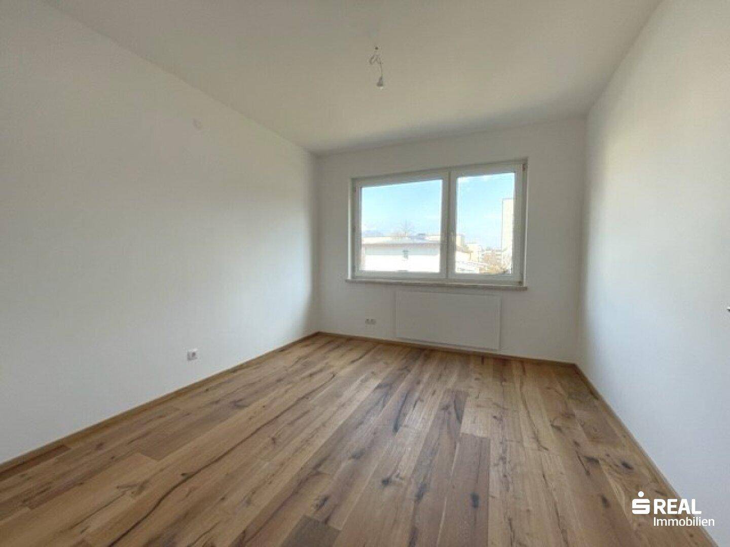 Heller und geräumiger Raum mit großem Fenster, das viel natürliches Licht spendet, und Holzfußboden.