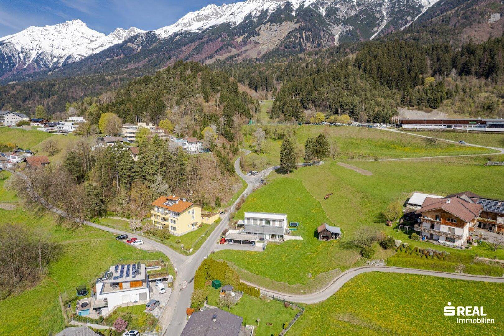 Luftaufnahme eines Wohngebiets mit modernen Häusern, grünen Wiesen und majestätischen Bergen.