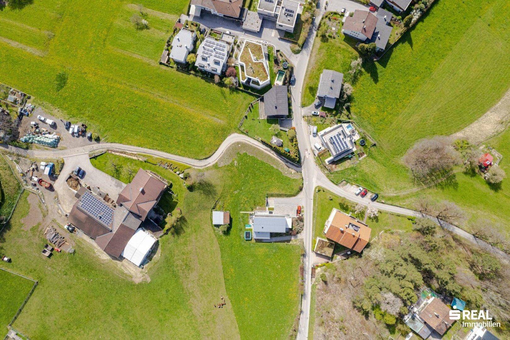Luftaufnahme eines Wohngebiets mit verschiedenen Häusern, Straßen und weitläufigen Grünflächen.