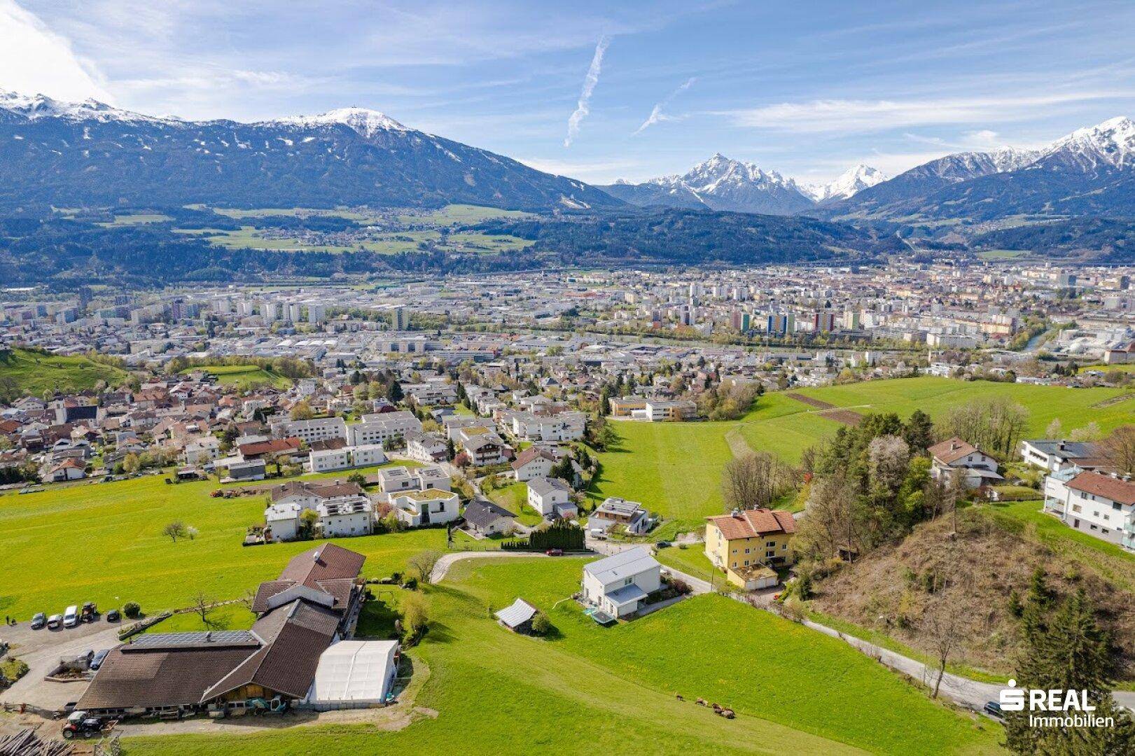 Umfassende Luftaufnahme der Stadtlandschaft mit grünen Hügeln und majestätischen Bergen im Hintergrund.