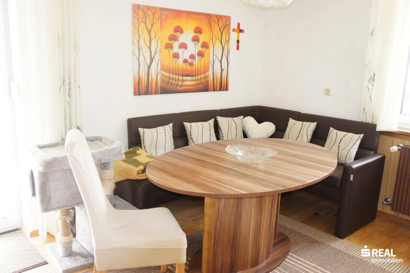 Gemütlicher Essbereich mit Eckbank, rundem Holztisch und farbenfrohem Wandbild.