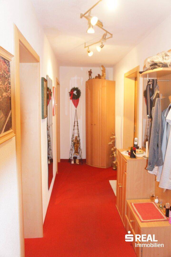 Langer Flur mit rotem Teppichboden und Holzschrank.