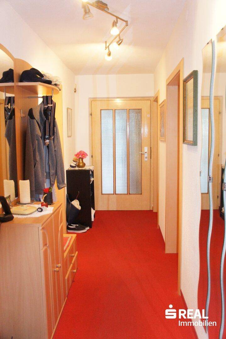 Flur mit rotem Teppichboden, Garderobe und Spiegelflächen.