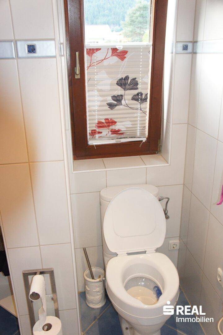 Separate Toilette mit Fenster und weißen Fliesen.