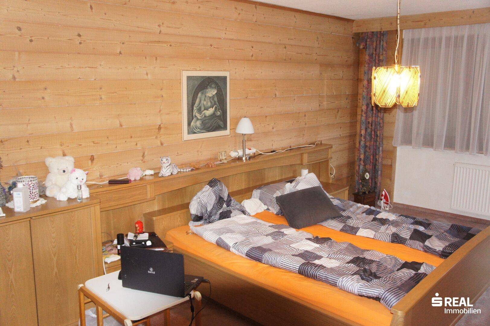 Schlafzimmer mit Holzwänden, Doppelbett und rustikaler Beleuchtung.