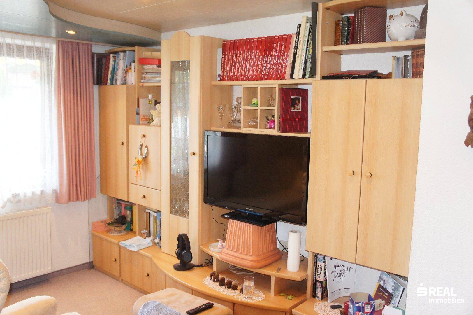 Wohnzimmer mit großer Schrankwand, Fernseher und Blick nach draußen.