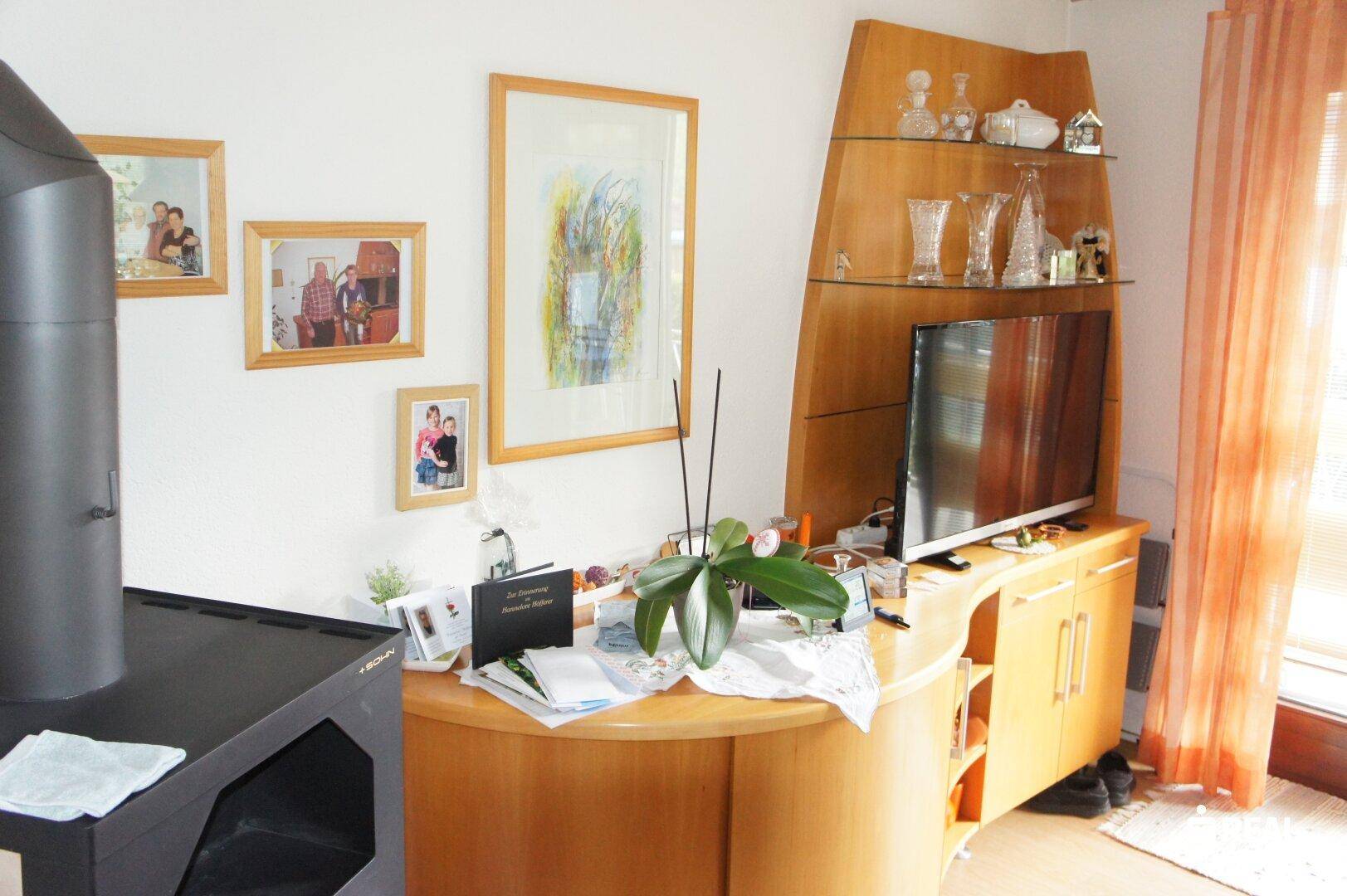 Wohnbereich mit Kaminofen, Holzmöbeln und Fenster mit Vorhängen.