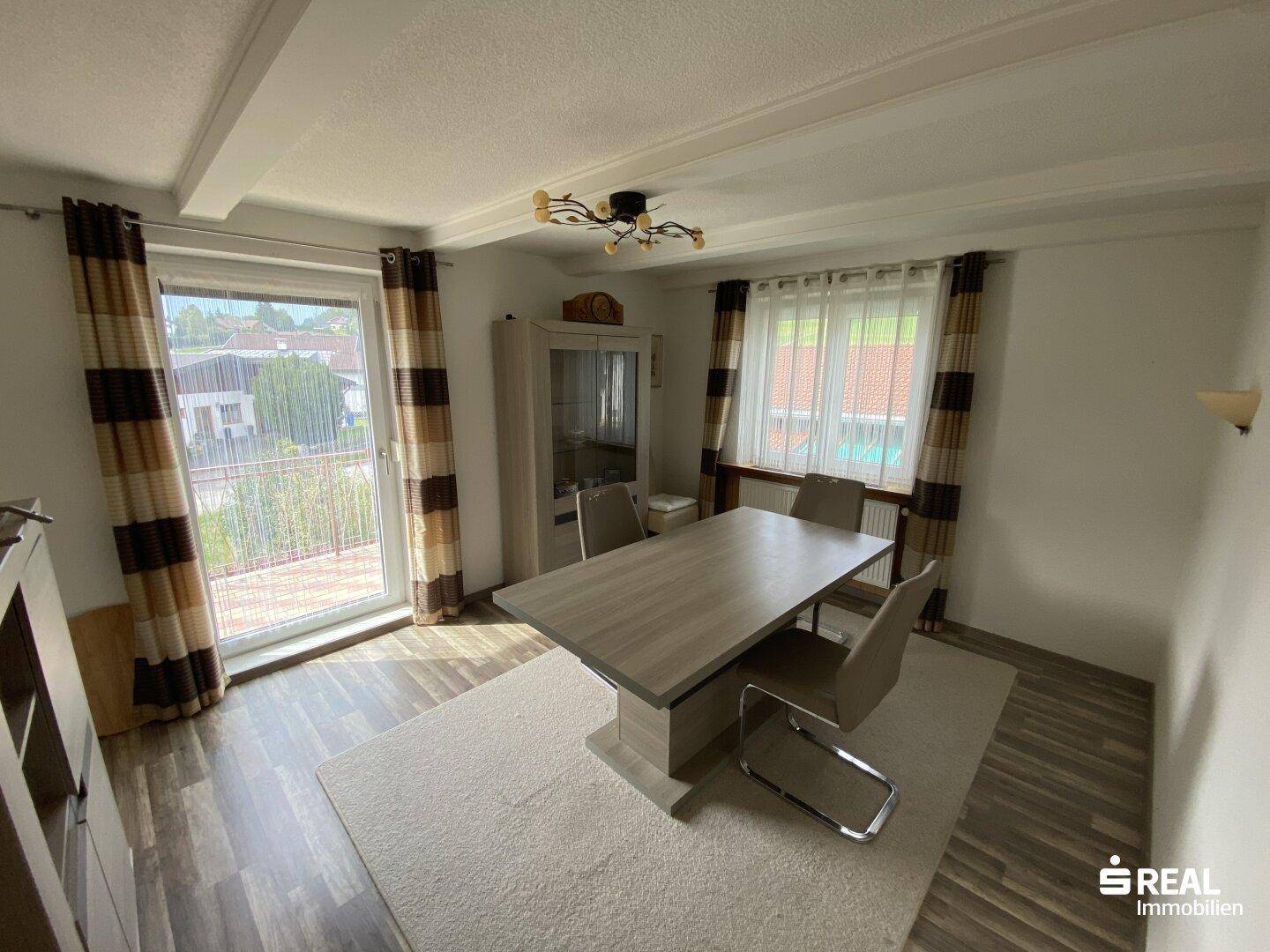 Heller Essbereich mit großem Tisch, Holzbalkendecke und Zugang zum Balkon.