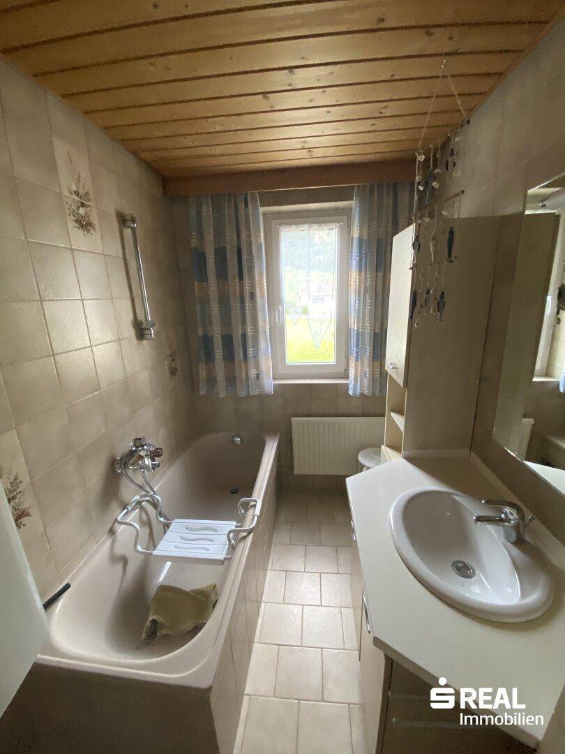 Badezimmer mit Badewanne, Waschbecken und Holzdecke.