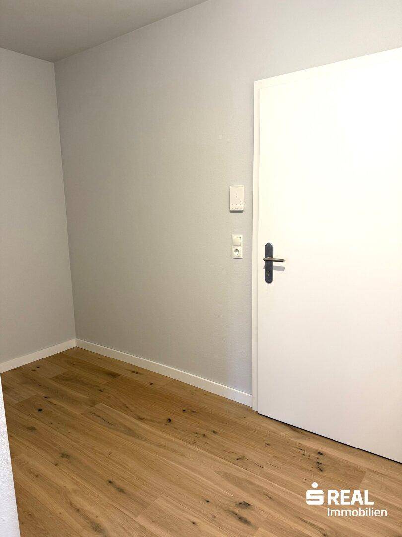 Ecke eines hellen Raumes mit Holzboden und einer modernen weißen Tür.