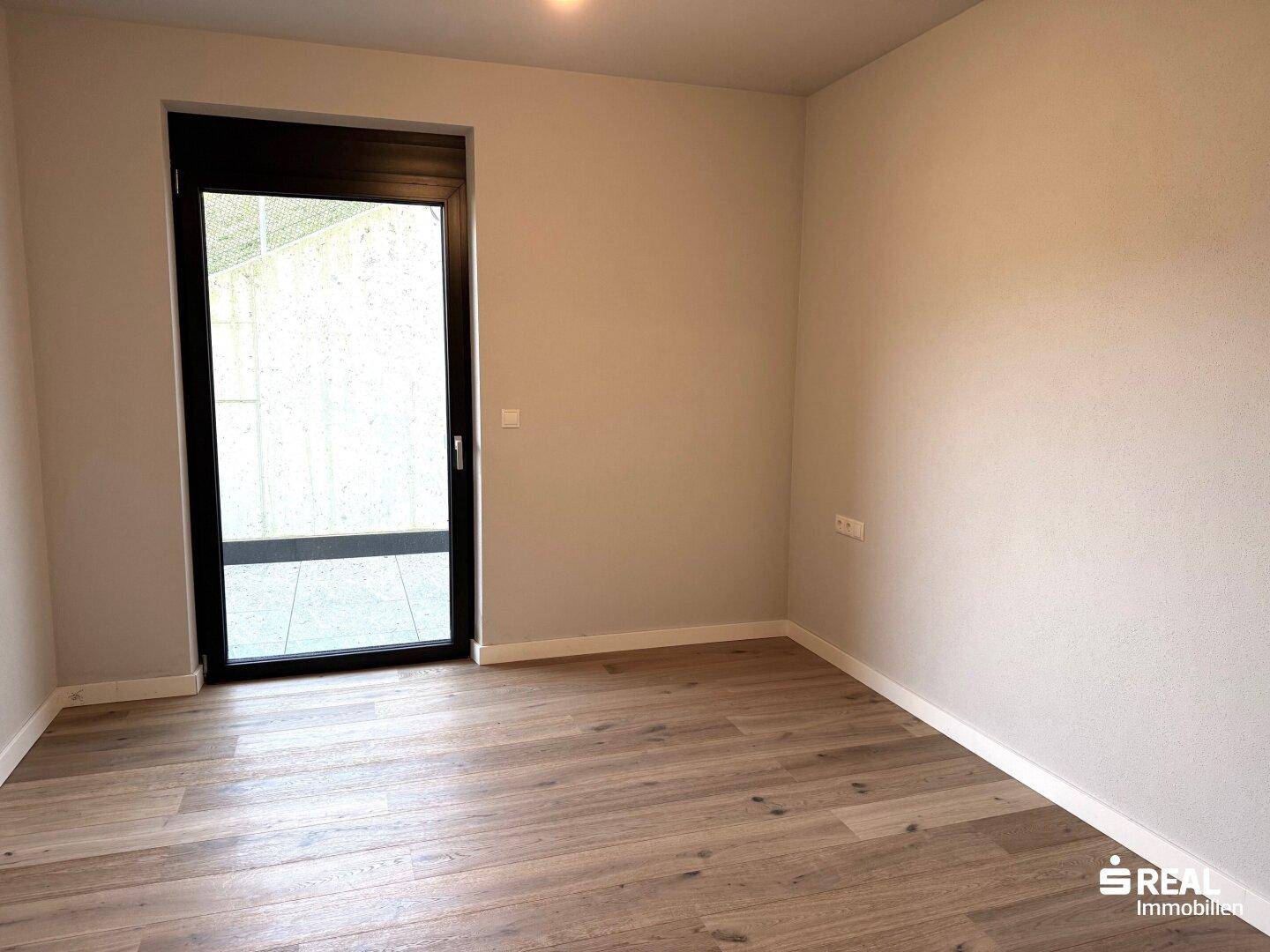 Kleinerer Raum mit Holzboden und Zugang zu einem Außenbereich, ideal als Schlafzimmer.