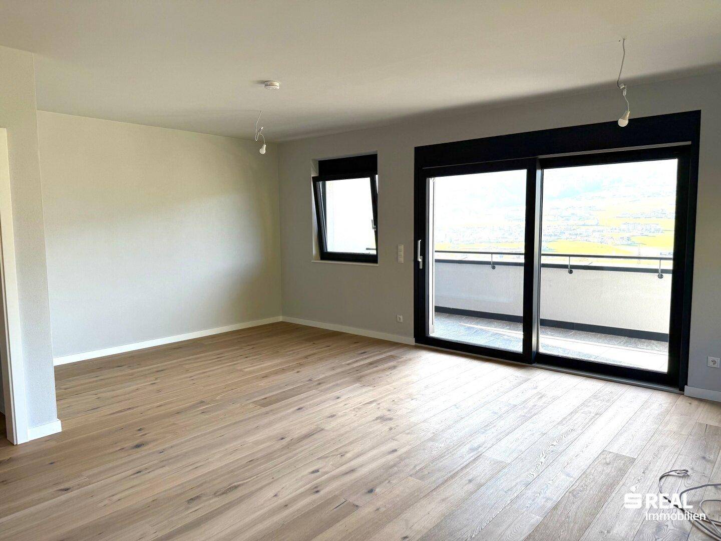 Lichtdurchfluteter Raum mit Holzboden und großem Schiebefenster zum Balkon.