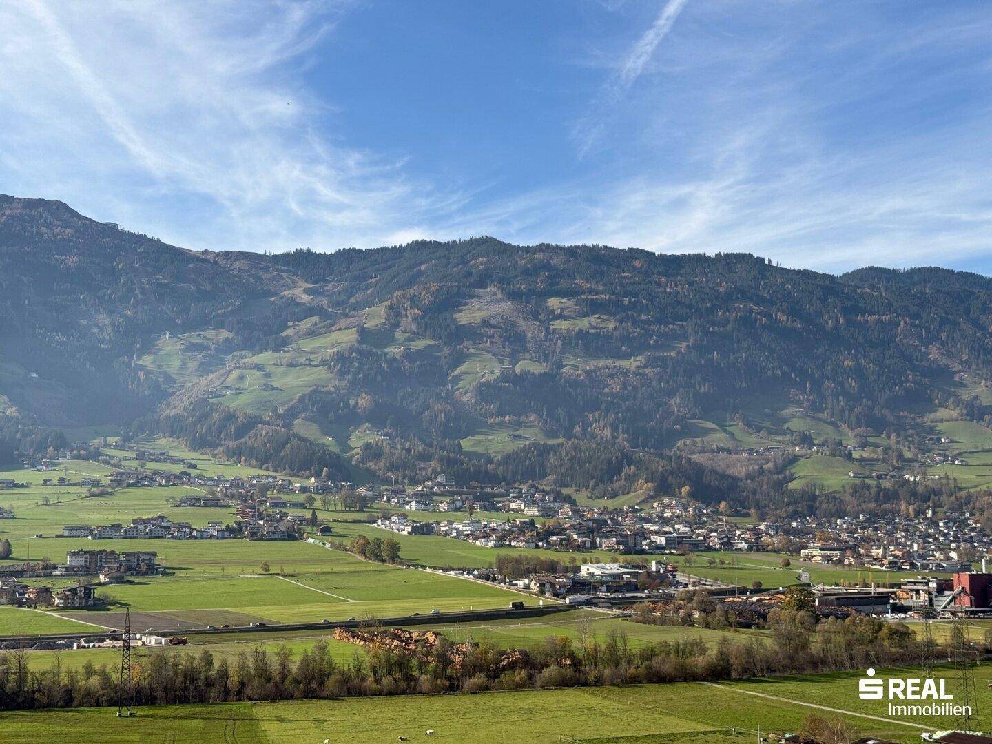 Malerischer Ausblick auf das weite Tal mit grünen Feldern, Bergen und einer kleinen Siedlung.