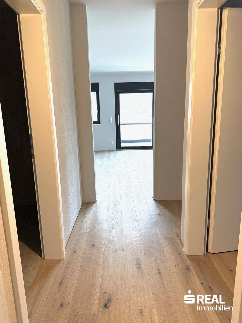 Heller Flur mit hochwertigem Holzparkettboden, der zu den lichtdurchfluteten Wohnbereichen führt.