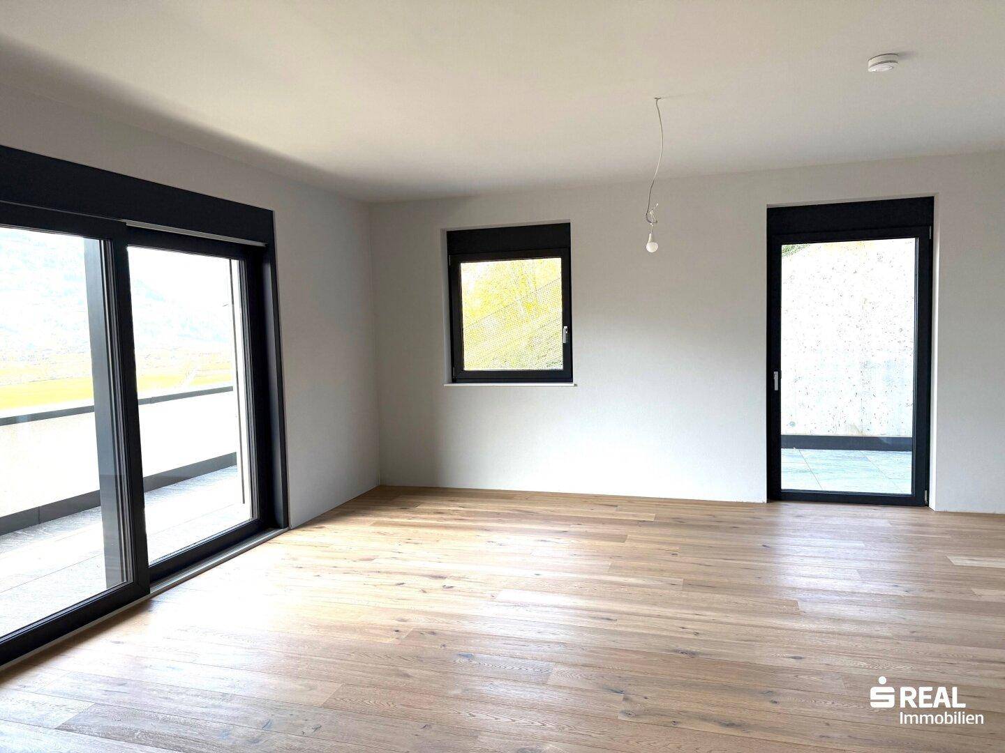 Geräumiges, helles Wohnzimmer mit Holzparkettboden und großem Schiebetürzugang zum Balkon.