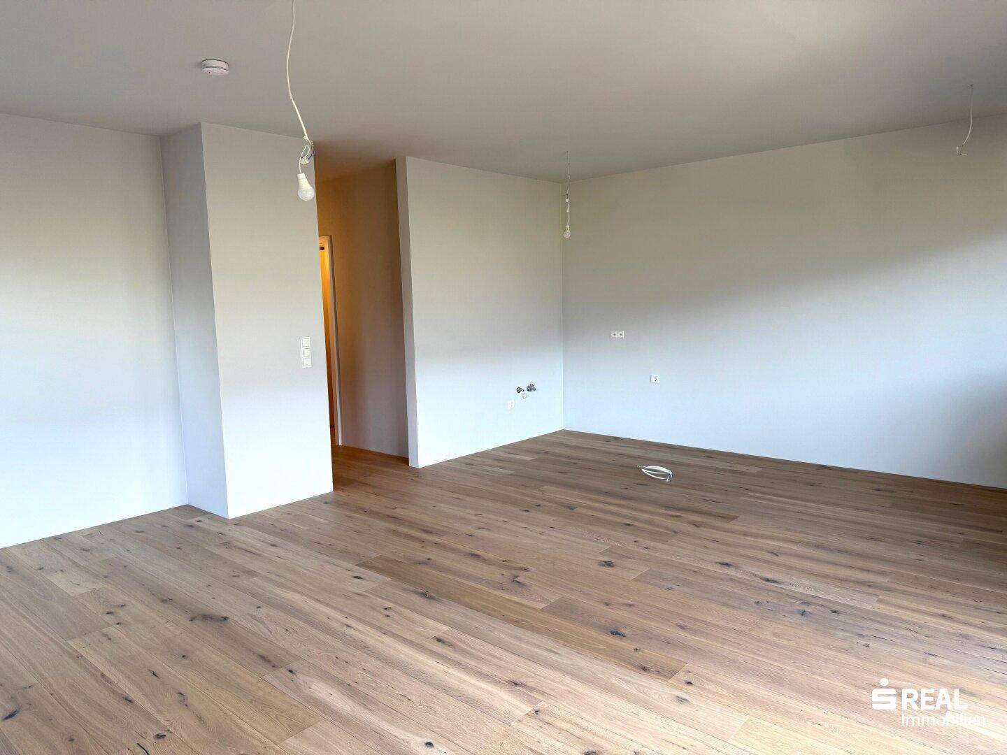 Lichtdurchfluteter Wohnbereich mit edlem Holzparkettboden, bereit für individuelle Einrichtungsideen.
