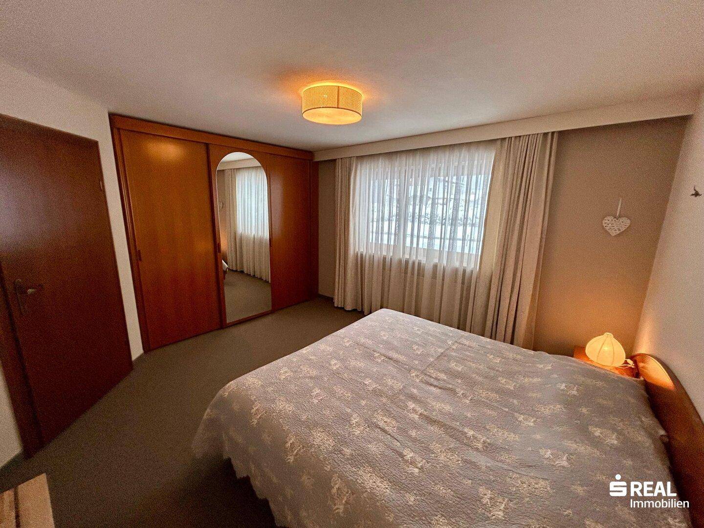 Schlafzimmer mit Doppelbett, Holzschrank mit Spiegeltür und Teppichboden.