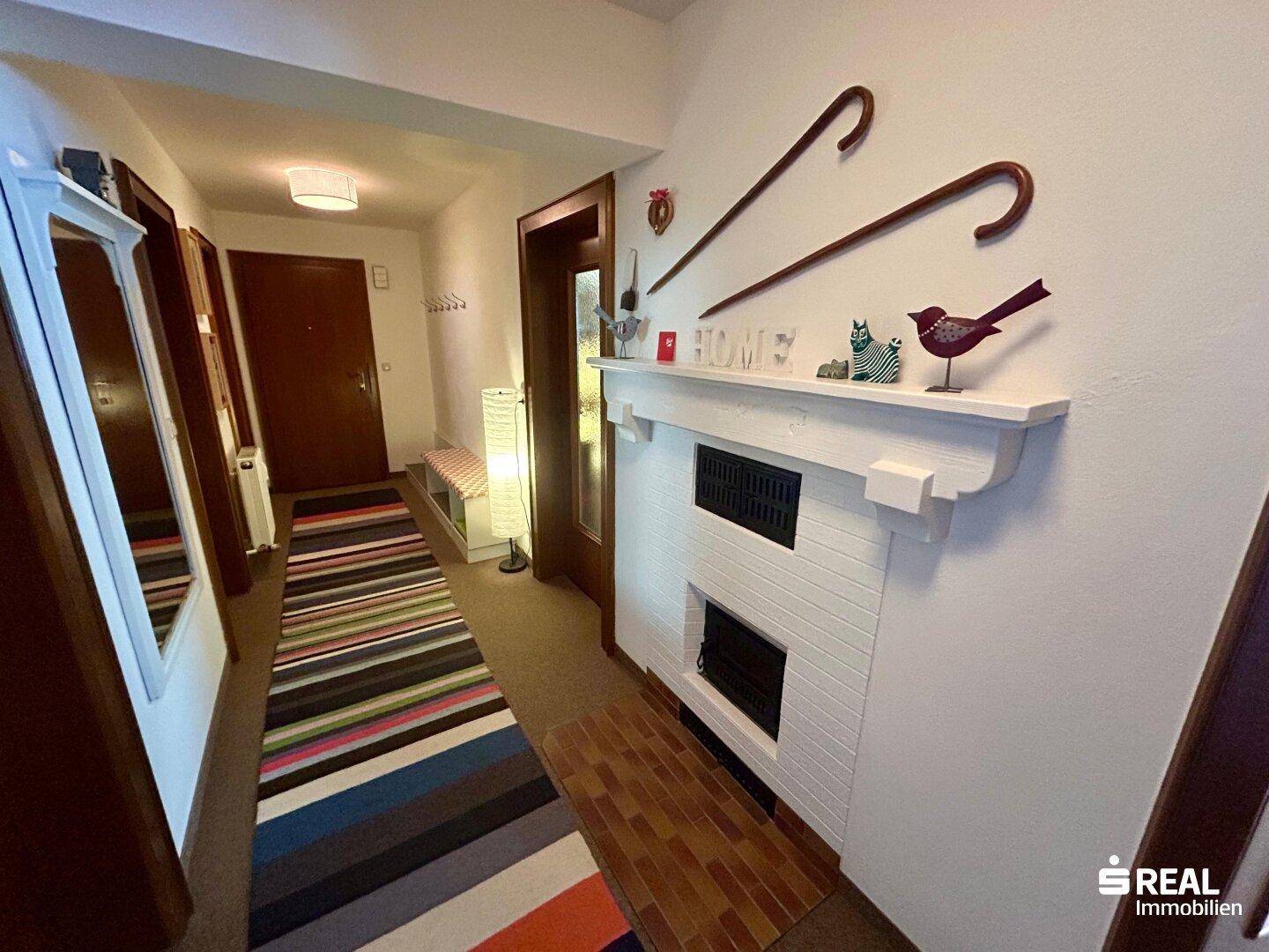 Flur mit Teppichboden, weißem Kamin und traditionellen Dekorationen.