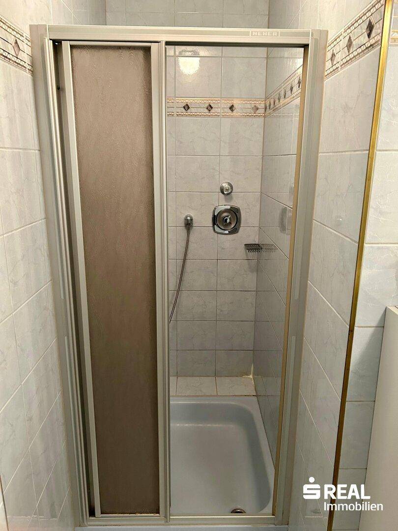 Duschkabine mit Schiebetür in einem gefliesten Badezimmer.