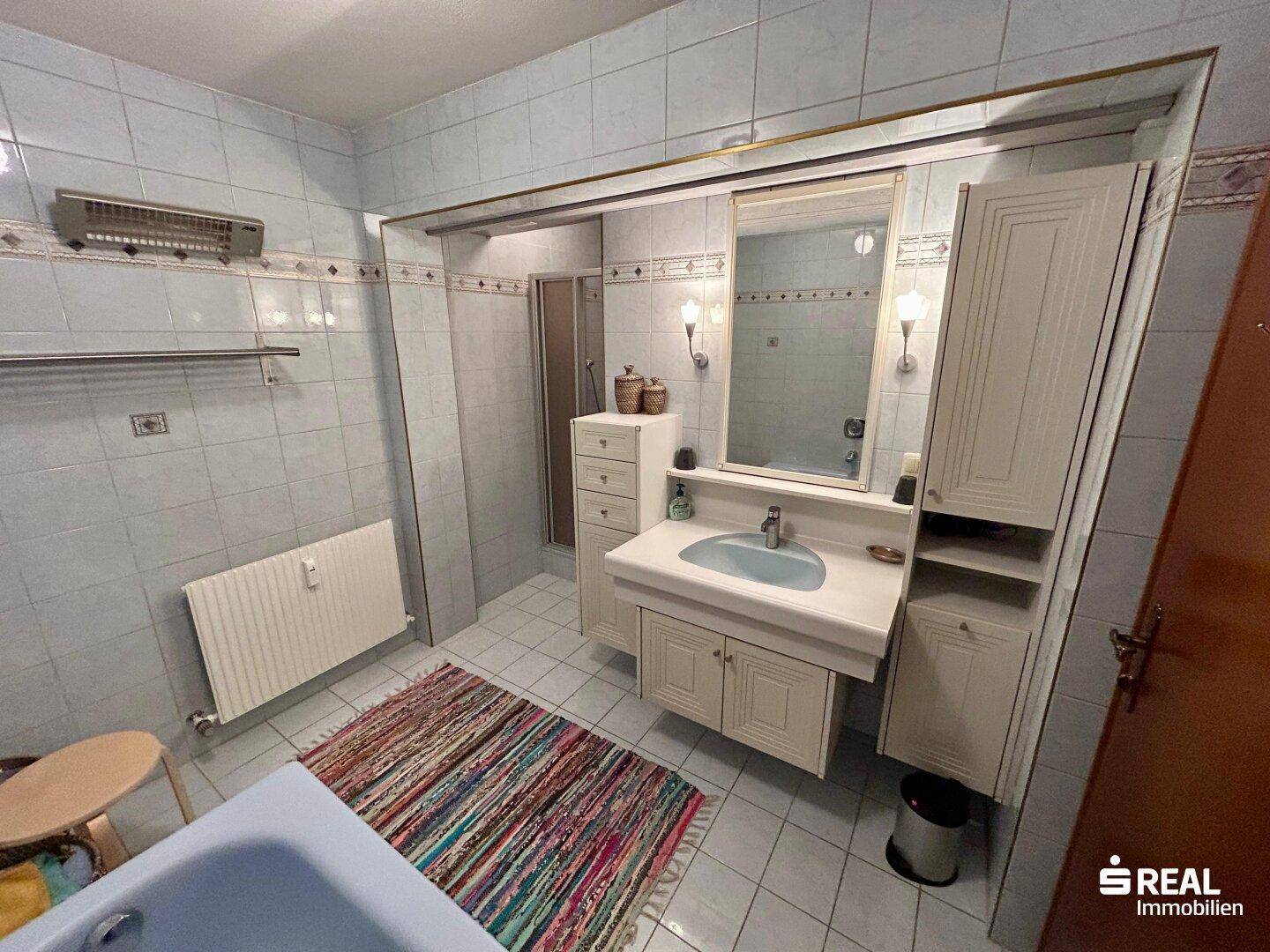 Badezimmer mit Waschtisch, Spiegel, Dusche und Badewanne, alles in hellblauen Fliesen.