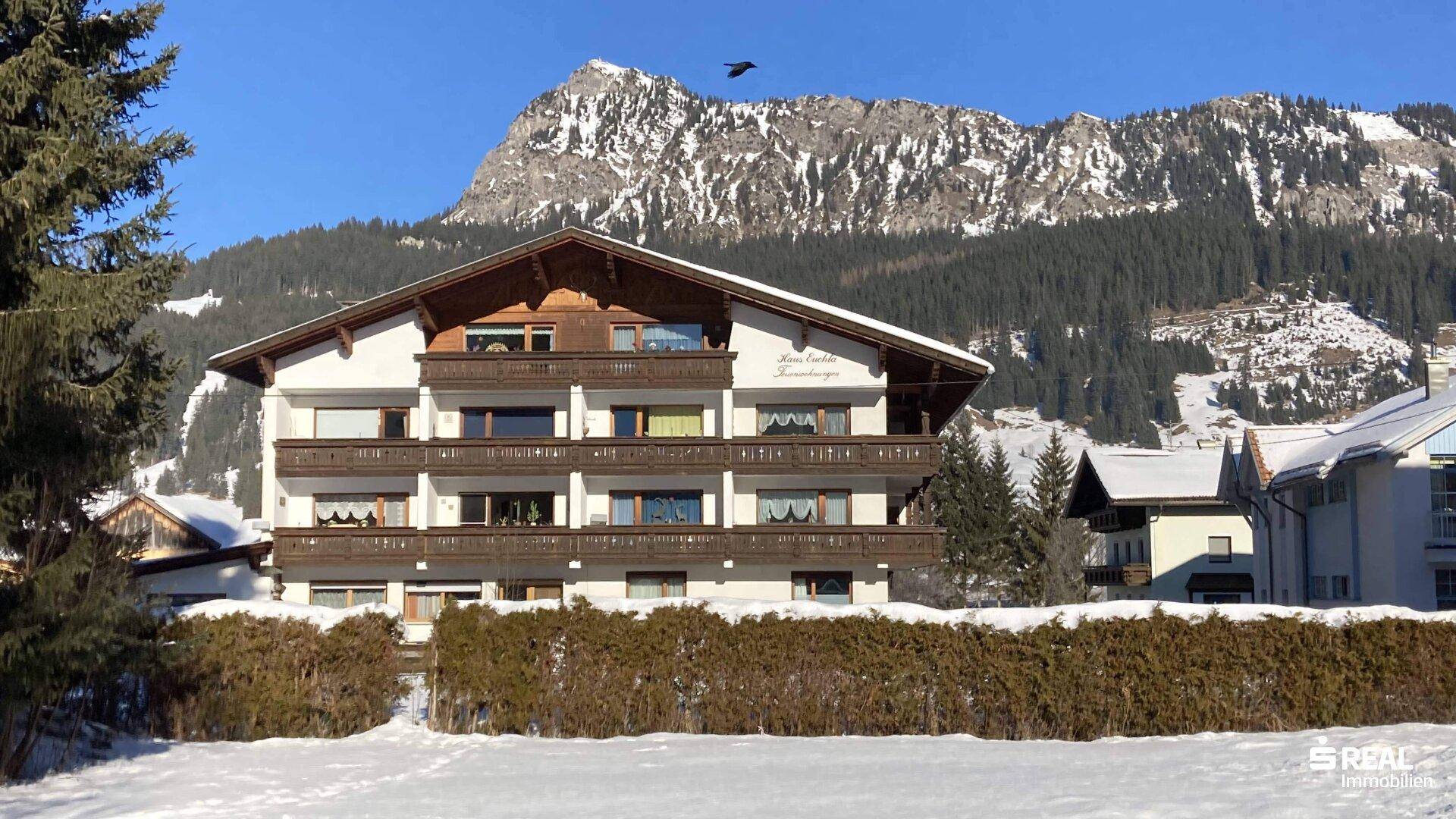 Mehrfamilienhaus in den Bergen mit Balkonen und schneebedeckter Landschaft.