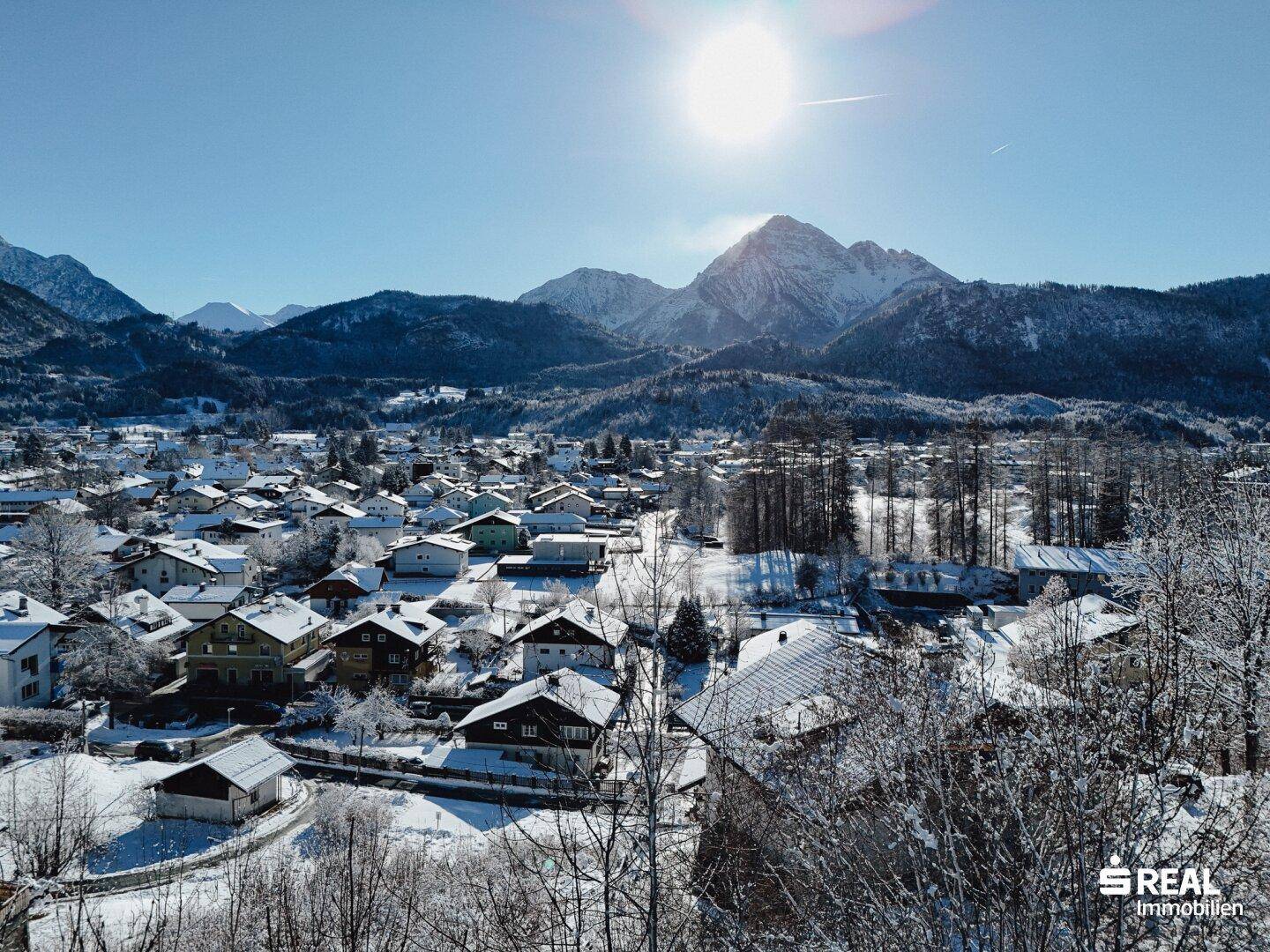 Luftaufnahme einer verschneiten Stadt mit Bergen im Hintergrund, die von der Wintersonne beleuchtet wird.