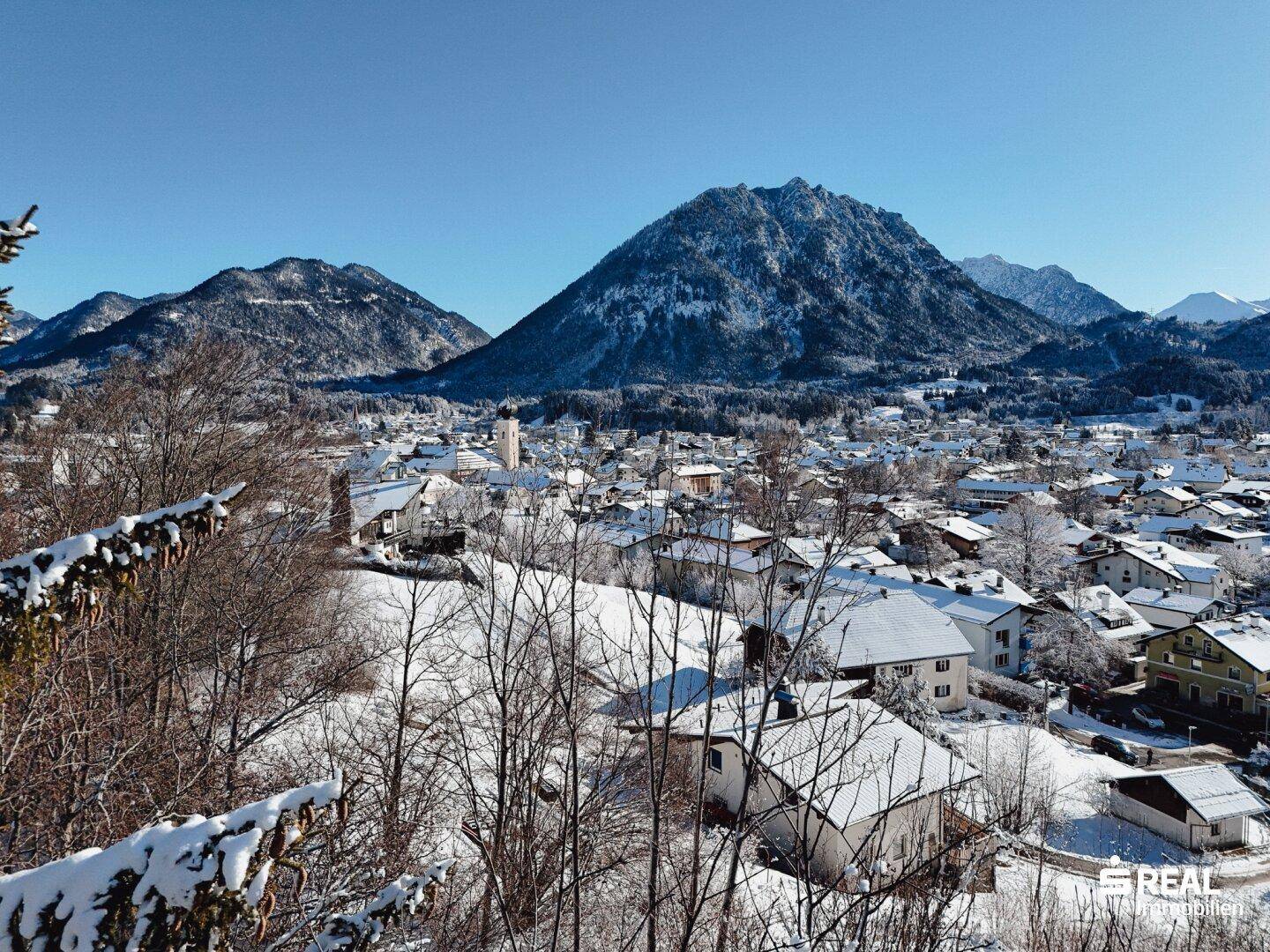Weitläufige Luftaufnahme einer verschneiten Stadt, eingebettet in eine Berglandschaft unter klarem Winterhimmel.