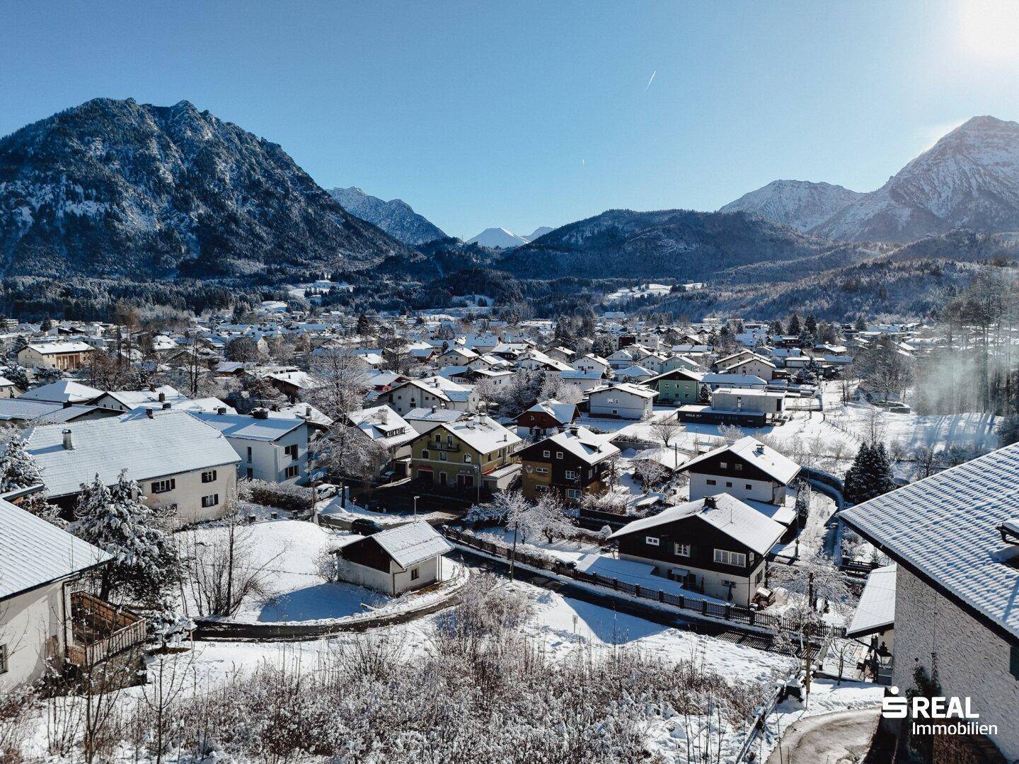 Panoramablick auf eine verschneite Stadt mit zahlreichen Häusern und einer beeindruckenden Bergkulisse.