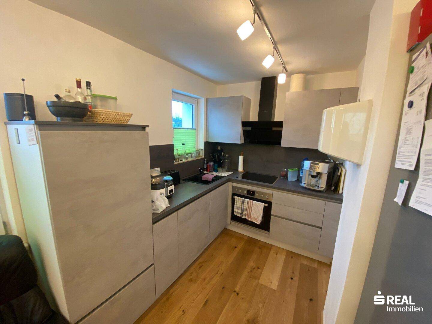 Moderne Einbauküche in Grau mit Holzfußboden und Fenster für natürliches Licht.
