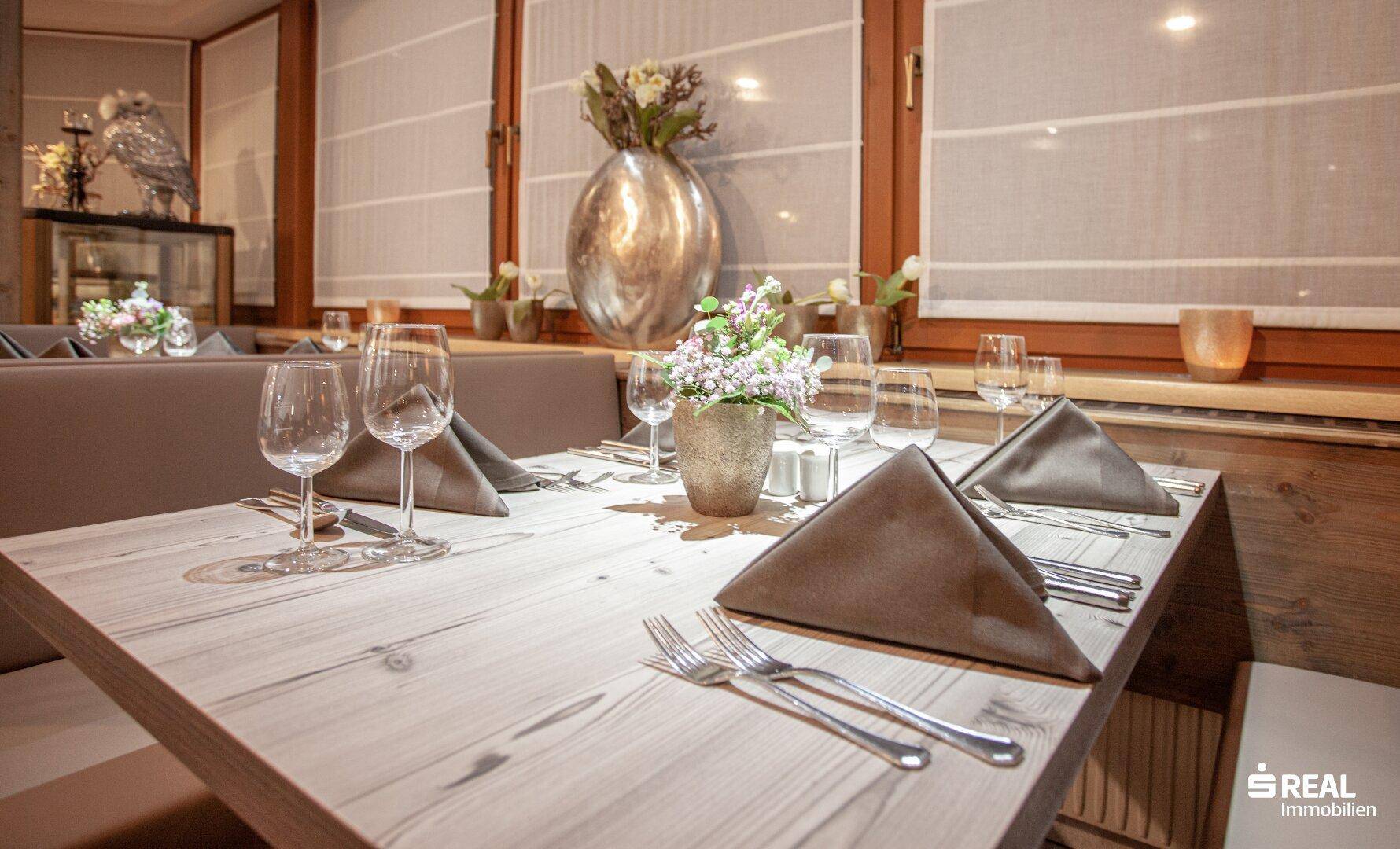 Detailansicht eines gedeckten Tisches im Restaurant mit Gläsern, Besteck und Blumen.